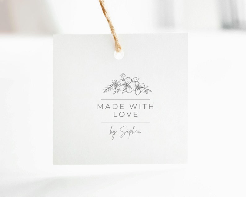 May include: A square white paper tag with a hole at the top and a brown twine string. The tag features a black line drawing of a floral arrangement above the text MADE WITH LOVE and the script name by Sophia, centered on the front surface.
