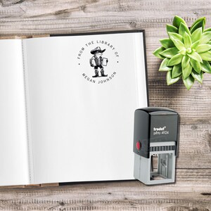 May include: A black and white stamp with a round design. The design features a cartoon cowboy holding a book and the text "From the Library of Megan Johnson".