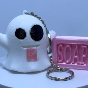 Pode incluir: Chaveiro de fantasma branco com uma l&iacute;ngua rosa para fora, segurando uma barra de sab&atilde;o rosa que diz "SOAP" em letras brancas.