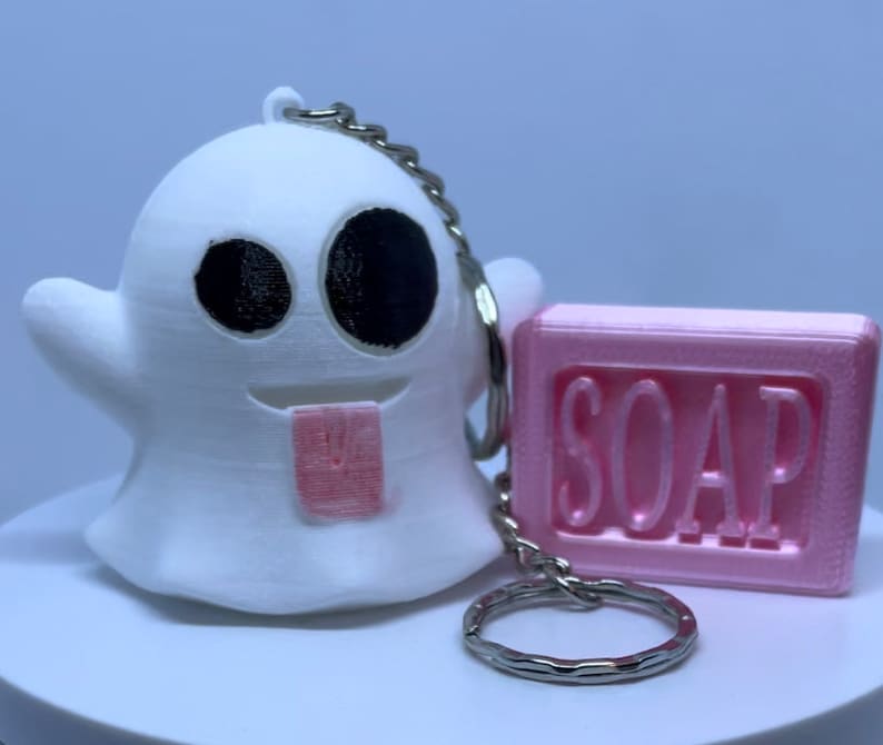 Pode incluir: Chaveiro de fantasma branco com uma l&iacute;ngua rosa para fora, segurando uma barra de sab&atilde;o rosa que diz "SOAP" em letras brancas.