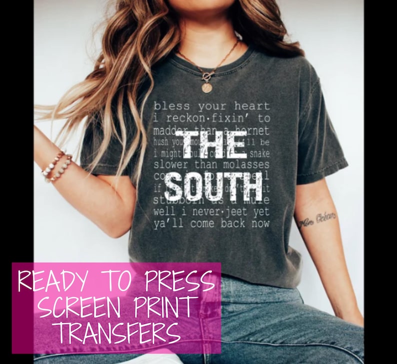 以下が含まれることがあります： 暗いグレーのTシャツに、白い文字で「Bless your heart I reckon fixin' to madder than a hornet hush you I might be slower than molasses if the South well I never jeet yet ya'll come back now」と書かれた、プレス可能なスクリーン印刷転写シートです。