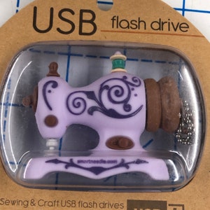 May include: Purple and brown sewing machine shaped USB flash drive with a decorative floral design. The drive is labeled "smartneedle.com". Sewing & Craft USB flash drives.