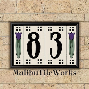 May include: Rectangular address plaque with the numbers "83" in black, set against a cream background. The plaque features purple tulip illustrations and a black frame. The text "MalibuTileWorks" is at the bottom.