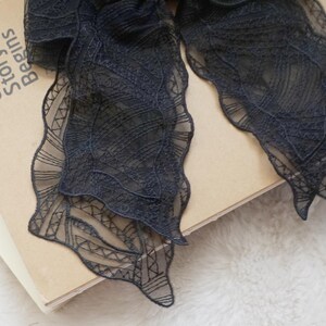 May include: Close-up of a dark navy blue lace ribbon with a scalloped edge, resting on a book. The book has the text "Our Story Begins" printed on the cover. The lace has a delicate, intricate pattern.