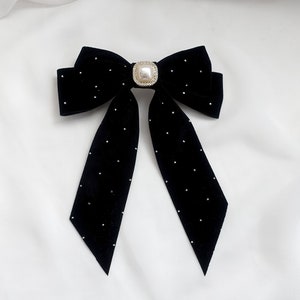 May include: A black velvet bow with a pearl-like button in the centre. The bow has small white dots throughout.