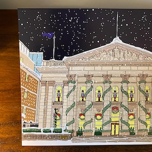 May include: A snowy night scene with a large building decorated with garlands and nutcracker figures. The building has a classical facade with columns and a pediment. The sky is dark blue with white snowflakes falling.