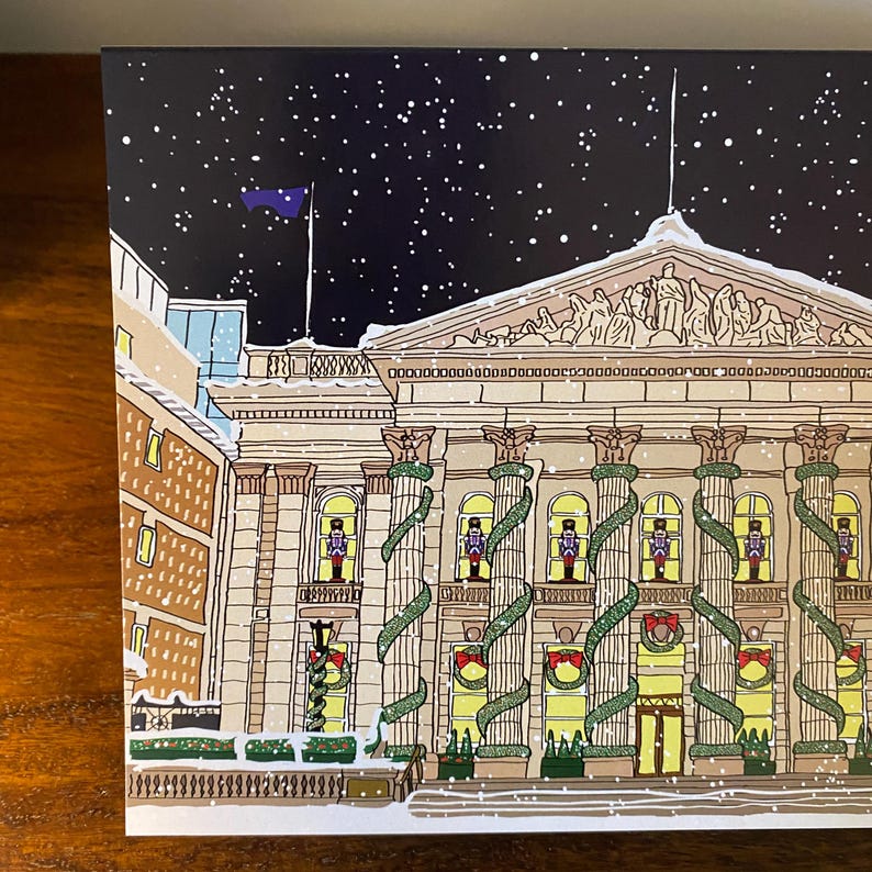 May include: A snowy night scene with a large building decorated with garlands and nutcracker figures. The building has a classical facade with columns and a pediment. The sky is dark blue with white snowflakes falling.
