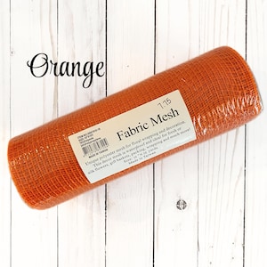 May include: A roll of orange fabric mesh for floral wrapping and decoration. The label reads "Fabric Mesh" and "Size: 10 x 10 yards". The mesh is made of polyester and is waterproof. The word "Orange" is written in cursive.