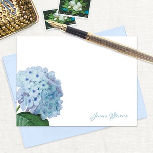 May include: A white card with a blue hydrangea illustration on the left side and the name "Jenna Stevens" written in cursive on the right side.