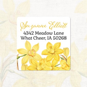 May include: A white square return address label with a floral design featuring yellow daffodils. The label includes the text "Suzanne Elliott", "4342 Meadow Lane", and "What Cheer, IA 50268".