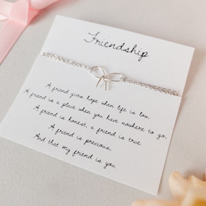 May include: A silver friendship bracelet with a bow charm and a card with the text "Friendship" and a poem about the importance of friendship.
