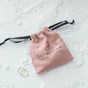 May include: A pink velvet pouch with a black drawstring and the text "lovassion inspirational jewellery". Two gold rings are visible outside the pouch.