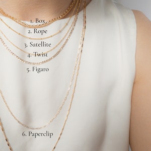 May include: A collection of seven gold necklaces with different chain styles, including box, rope, satellite, twist, figaro, paperclip, and bar designs. The necklaces are displayed against a white background.