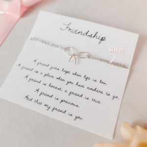 May include: A silver friendship bracelet with a bow charm and a card with the text "Friendship" and a poem about the importance of friendship.