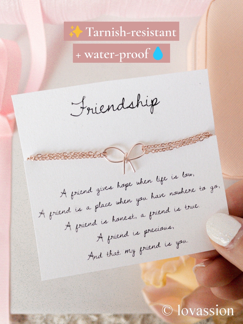 May include: A white card with the word "Friendship" written in black cursive. The card features a quote about friendship and a delicate gold chain necklace with a bow charm. The card is tarnish-resistant and water-proof.