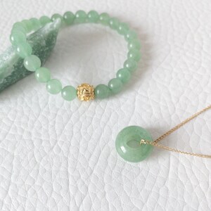 May include: A jade jewelry set featuring a beaded bracelet with a gold accent bead and a pendant necklace. The pendant is a circular jade stone on a gold chain. The bracelet and pendant are a light green color.