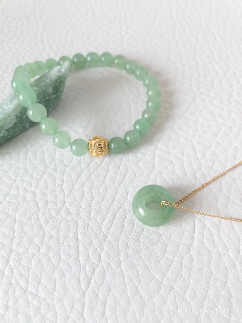 May include: A jade jewelry set featuring a beaded bracelet with a gold accent bead and a pendant necklace. The pendant is a circular jade stone on a gold chain. The bracelet and pendant are a light green color.