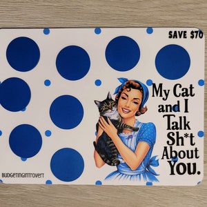 May include: A white card with blue polka dots and a retro-style illustration of a woman holding a cat. The text on the card reads "My Cat and I Talk Sh*t About You." and "SAVE &pound;70".