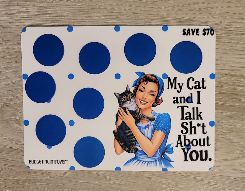May include: A white card with blue polka dots and a retro-style illustration of a woman holding a cat. The text on the card reads "My Cat and I Talk Sh*t About You." and "SAVE &pound;70".