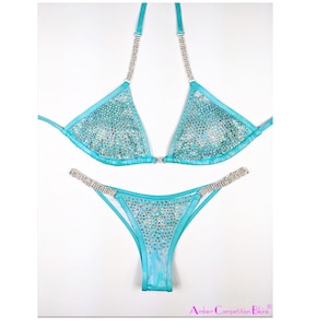 May include: A turquoise bikini with crystal embellishments. The bikini top has a triangle shape and the bottom is a high-cut style. The bikini is decorated with clear crystals.