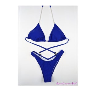 May include: A royal blue bikini set. The top features rhinestone straps and a clasp closure. The bottoms are high-cut with a criss-cross design. The set is presented against a white backdrop.