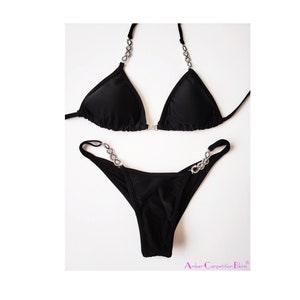 May include: A black bikini set with rhinestone accents. The triangle top and thong-style bottoms are displayed on a white background. The straps of the top and sides of the bottoms feature a decorative rhinestone chain.