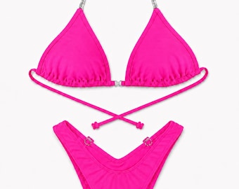 Könnte beinhalten: Ein leuchtend pinkfarbener Bikini bestehend aus einem Triangel-Oberteil mit silberfarbenen Kettenträgern und einem Mittelstück. Das passende Bikini-Unterteil mit hohem Beinausschnitt hat einen V-förmigen Bund mit zwei kleinen silbernen Ringdetails.