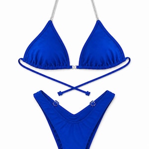 May include: A vibrant royal blue bikini set featuring a triangle top with silver chain straps and a central connector. The matching high-cut bikini bottoms include a V-shaped waistband with small silver hardware accents on each side of the hips.