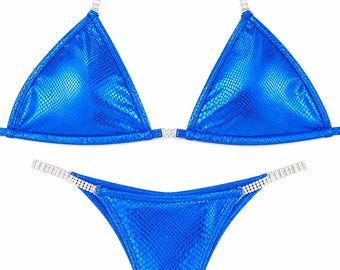 Puede incluir: Un conjunto de bikini azul brillante con un patrón texturizado de piel de serpiente. La parte superior triangular y la inferior de corte alto están acentuadas con tiras de cadena de diamantes de imitación plateados que unen las piezas.
