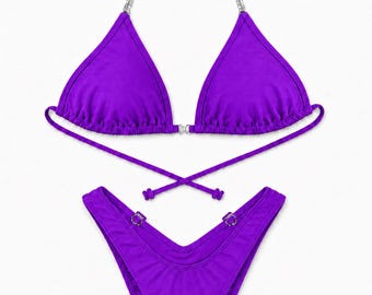 Könnte beinhalten: Ein leuchtend violettes Bikini-Set bestehend aus einem Triangel-Oberteil mit silbernen Kettenträgern und einem Mittelstück sowie einem hoch geschnittenen Bikini-Unterteil mit silbernen Ringdetails an den Hüften und langen Bindebändern.