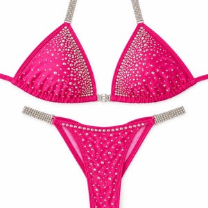 Könnte beinhalten: Ein leuchtend pinkfarbener Bikini bestehend aus einem Triangel-Oberteil und einem passenden Unterteil. Beide Teile sind mit verstreuten, klaren Strasssteinen besetzt. Das Oberteil hat silberfarbene, mit Strass verzierte Träger.