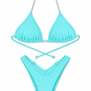 May include: A bright turquoise two-piece bikini set featuring a triangle top with silver-toned chain straps and wrap-around ties. The matching high-cut bikini bottom includes silver-toned ring hardware details at the front waistline.