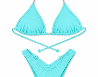 Könnte beinhalten: Ein leuchtend türkisfarbener Bikini-Zweiteiler bestehend aus einem Triangel-Oberteil mit silberfarbenen Kettenträgern und Wickelbändern. Das passende hoch geschnittene Bikini-Unterteil ist vorne am Bund mit silberfarbenen Ringen versehen.