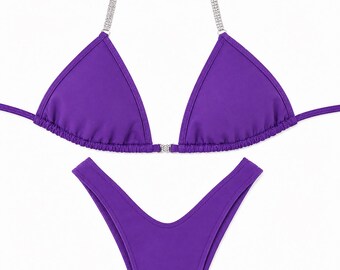 Könnte beinhalten: Ein leuchtend violettes zweiteiliges Bikini-Set bestehend aus einem Triangel-Oberteil mit dünnen Trägern, die mit Reihen aus klaren Strasssteinen verziert sind, und einem passenden hoch geschnittenen Unterteil mit Strass-Element.