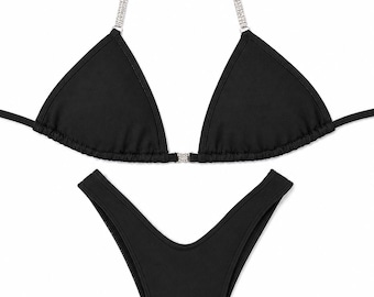 Könnte beinhalten: Ein schwarzer zweiteiliger Bikini mit einem Triangel-Oberteil, das dünne, mit silberfarbenen Strasssteinen verzierte Träger und ein kleines Strass-Verbindungsstück in der Mitte aufweist. Das Unterteil hat einen hohen Beinausschnitt.