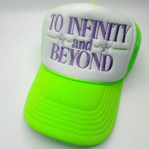 May include: A neon green and white trucker hat with the phrase "TO INFINITY and BEYOND" embroidered in purple. The hat features a curved brim and a mesh back for breathability. The text is centered on the front panel, with two star accents.