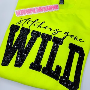 May include: A neon yellow sweatshirt with the words "Stitchers gone WILD" in black sequined letters. A pink and white label that says "WONDERFUL DAY BOUTIQUE" is above the text.