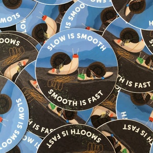 May include: A collection of round stickers with a blue background and white text that reads "Slow is Smooth, Smooth is Fast". The stickers feature a cartoon illustration of a snail with a shell and a body that is decorated with colorful details.