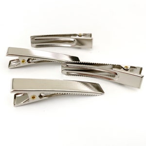 May include: Three silver metal hair clips of different sizes. The clips are all in focus and are arranged in a row on a white background.