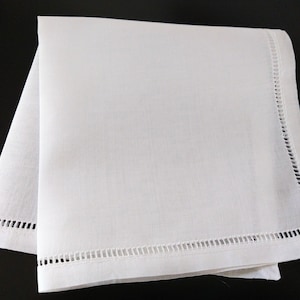 May include: A folded white linen napkin with a decorative cutwork border. The napkin is square and appears to be made of a fine, smooth fabric. The cutwork border is a series of small, evenly spaced rectangular openings.
