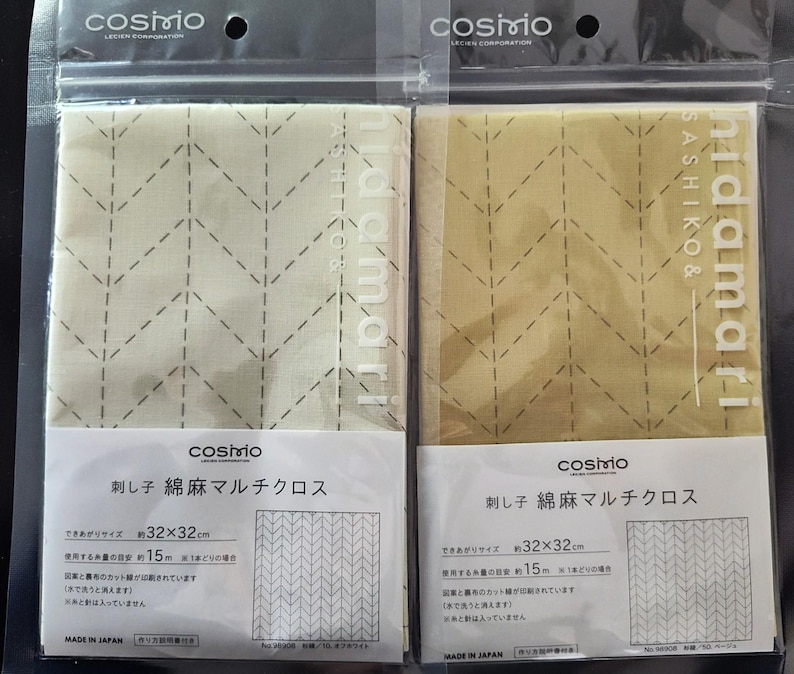 K&ouml;nnte beinhalten: Zwei verpackte Stoffquadrate mit einem gesteppten Zickzackmuster. Der Stoff ist beige und olivgr&uuml;n, mit dem Text "hidamari" und japanischem Text auf der Verpackung. Jedes Quadrat misst ca. 32 x 32 cm.