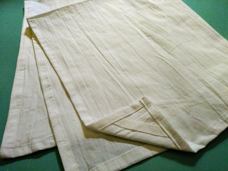 May include: Three white cotton dish towels folded together. The towels have a textured, ribbed surface.