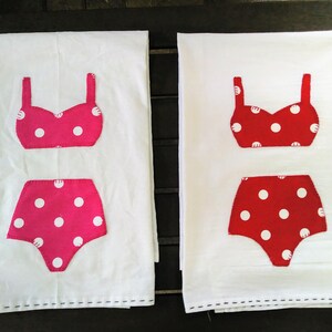 May include: Two white tea towels with red and pink polka dot swimsuit designs. The swimsuits are appliqued on the towels.