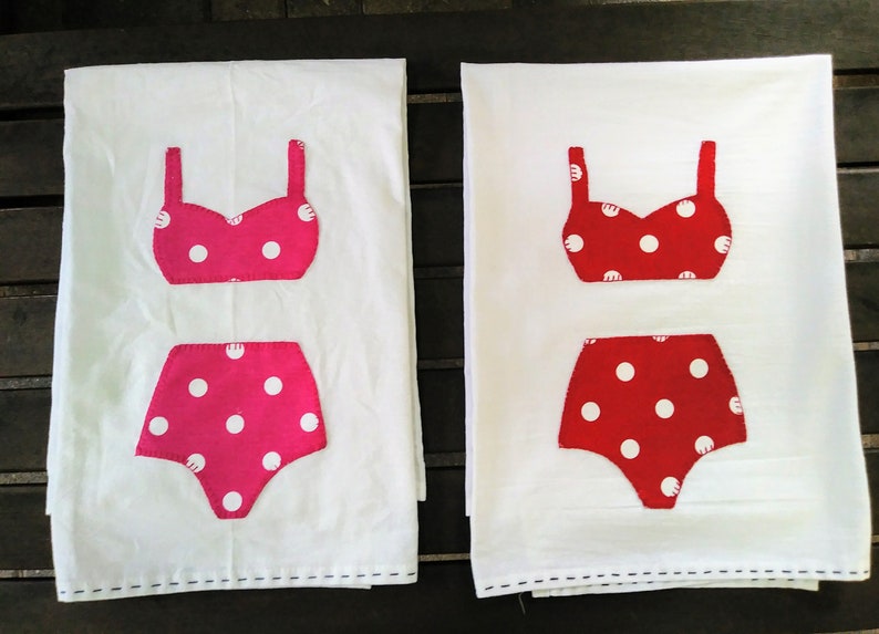 May include: Two white tea towels with red and pink polka dot swimsuit designs. The swimsuits are appliqued on the towels.