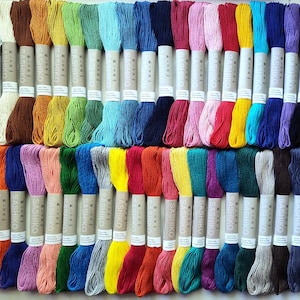 May include: A collection of colorful embroidery floss skeins, arranged in rows. The floss is in a variety of colors, including white, brown, yellow, green, blue, pink, red, and purple. Each skein is labeled with the brand name.