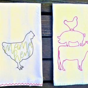 May include: Two white tea towels with embroidered designs. The left towel has a yellow chicken silhouette with the text "mama hen" inside. The right towel has a pink cow, pig, and chicken silhouette stacked on top of each other.