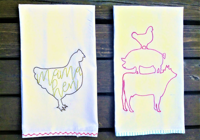 May include: Two white tea towels with embroidered designs. The left towel has a yellow chicken silhouette with the text "mama hen" inside. The right towel has a pink cow, pig, and chicken silhouette stacked on top of each other.