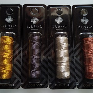 May include: Four spools of embroidery floss in gold, gray, silver, and brown, packaged in clear plastic with black labels that read "にしきいと nishikiito" and "cosmo".