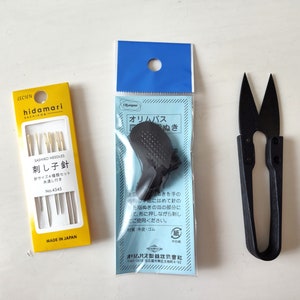 May include: A set of three yellow and gold sewing needles in a clear plastic package with a yellow label that reads "SASHIKO NEEDLES 刺し子針" and "MADE IN JAPAN". A blue and white package with a black thimble and a black pair of small scissors.
