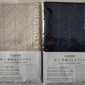 K&ouml;nnte beinhalten: Zwei Stoffquadrate, eines beige und eines marineblau, mit einem gen&auml;hten Zickzackmuster. Jedes ist mit einem Etikett versehen, auf dem "Cotton/Linen Sashiko Fabric" steht. Die fertige Gr&ouml;&szlig;e betr&auml;gt ca. 32 cm x 32 cm.